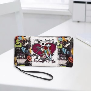 May include: A rectangular wallet with a wrist strap featuring a collage of characters from The Nightmare Before Christmas. The center displays Jack Skellington and Sally in front of a red heart with the text We're Simply Meant to be.