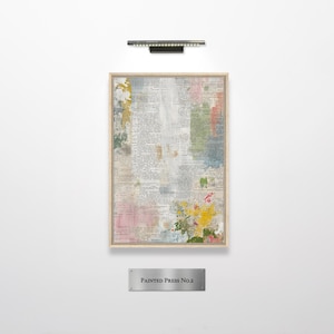 May include: A rectangular framed artwork titled PAINTED PRESS No.2 featuring a vintage dictionary page background overlaid with abstract patches of yellow, pink, green, and grey paint. The piece is displayed under a horizontal metal light fixture.