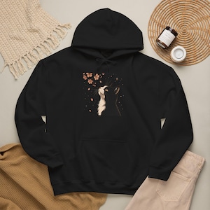 Peut inclure: Un sweat à capuche noir orné d'une illustration représentant un chat noir et blanc regardant vers le haut des fleurs de cerisier roses et de petites étoiles. Le sweat possède une poche kangourou, des manches longues et des cordons noirs.