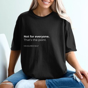 May include: A black short-sleeved t-shirt featuring white text on the chest that reads: Not for everyone. That's the point. MEASURED SELF. The garment has a crew neckline and a relaxed fit, constructed from a solid black fabric.