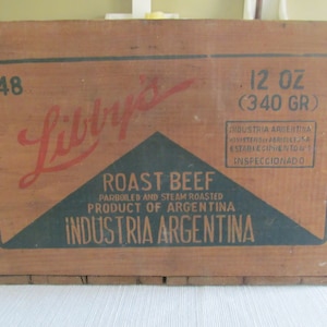 May include: A wooden box with a label that reads "Lilly's Roast Beef Parboiled and Steam Roasted Product of Argentina Industria Argentina 12 oz (340 gr)". The box is brown with black and green lettering.