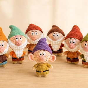 May include: A collection of seven small, handmade crochet dolls shaped like gnomes. Each figure features a pointed hat in various colors, including orange, green, red, brown, and purple, paired with a white beard, round nose, and simple clothing.