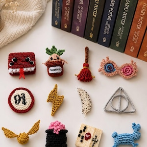 May include: A collection of twelve small, crocheted items including a red monster book, a potted mandrake, a broomstick, pink glasses, a 9 3/4 sign, a yellow lightning bolt, a white feather, a silver triangle symbol, a golden snitch, a black cauldron, a letter, and a blue rabbit.