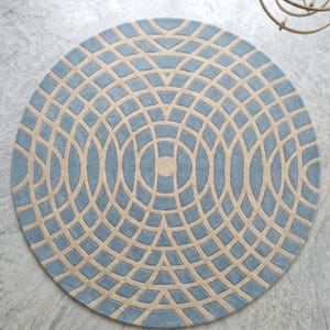 May include: A circular area rug featuring a repeating geometric pattern of light blue and cream-colored segments. The design consists of concentric circles intersected by radiating lines, creating a grid-like structure across the entire surface.