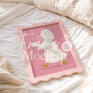 May include: A light pink scalloped picture frame containing an illustration of a white duck wearing a white bathrobe and a towel on its head while holding a cup of coffee. The text ISO DIN Frame Mockup and PSD File is overlaid on the image.
