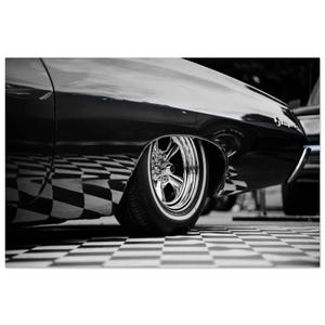 Könnte beinhalten: Ein Schwarz-Weiß-Foto, das das Seitenprofil eines Oldtimers mit einem polierten Chromrad und Reifen zeigt. Die Karosserie weist eine reflektierende Oberfläche auf, die ein schwarz-weißes Schachbrettmuster auf dem Boden unter dem Fahrzeug spiegelt.