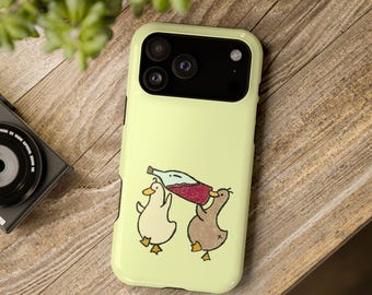 Puede incluir: Una funda de smartphone de color amarillo pálido con una ilustración gráfica de dos patos, uno blanco y otro marrón, sosteniendo una botella de vino tinto entre ambos. La funda tiene un área de recorte negra para la cámara.