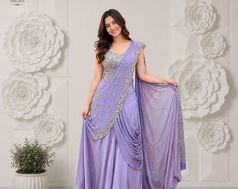 Puede incluir: Un vestido sin mangas de color lavanda con un corpiño ajustado con bordados plateados y una falda drapeada. La prenda presenta una silueta fluida hasta el suelo con intrincados abalorios a lo largo del hombro y la cintura, creando un efecto de capas.