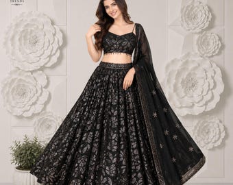 Puede incluir: Un conjunto de lehenga choli negro que presenta un top corto sin mangas y una falda larga hasta el suelo con un patrón de hojas doradas metálicas. El conjunto incluye una dupatta negra transparente con bordados dorados en los bordes.
