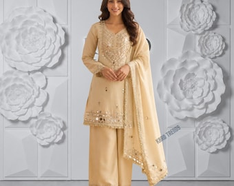 Puede incluir: Un conjunto beige de tres piezas que consta de una túnica de manga larga, pantalones anchos y una dupatta a juego. La túnica presenta bordados intrincados y detalles de espejos en el escote y el dobladillo. El texto KRRO TRENDS es visible.