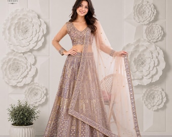 Puede incluir: Un conjunto de lehenga choli malva con blusa de cuello en V y falda larga hasta el suelo, con intrincados bordados geométricos dorados y detalles de lentejuelas, junto a una dupatta de red transparente a juego sobre el hombro.