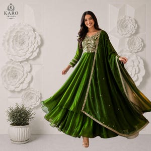 Puede incluir: Un vestido largo de color verde oscuro con un corpiño ajustado con intrincados bordados dorados, mangas largas y falda acampanada. El conjunto incluye una dupatta transparente a juego sobre el hombro, adornada con un borde dorado y detalles.