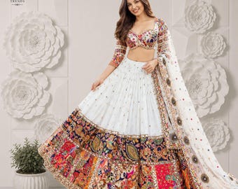 Puede incluir: Un conjunto de lehenga choli blanco que incluye una blusa corta y una falda larga con un borde ancho y multicolor estilo patchwork. El borde muestra intrincados patrones florales y de cachemira en rojo, azul y dorado, con detalles de espejos.