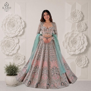 Puede incluir: Un conjunto de lehenga en verde salvia y rosa empolvado que incluye un top tipo bustier con escote coraz&oacute;n, adornado con cuentas y bordados, una falda larga acampanada a juego y un dupatta verde claro transparente sobre los brazos.
