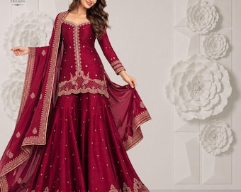 Puede incluir: Un conjunto sharara color granate profundo que presenta una túnica de manga larga y pantalones anchos con intrincados bordados dorados. El conjunto incluye un dupatta transparente a juego con un borde decorativo. El texto KARO TRENDS es visible.