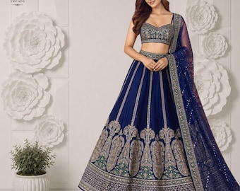 Puede incluir: Un conjunto lehenga azul profundo que incluye una blusa sin mangas con escote corazón y una falda larga, ambos adornados con intrincados bordados en plata y oro, junto con una dupatta transparente a juego con borde decorativo y espejos.