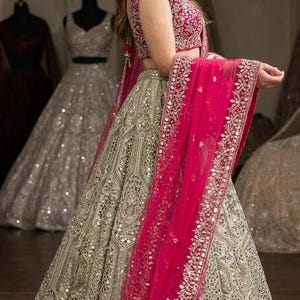 May include: A floor-length lehenga skirt in a metallic gold hue with intricate embroidery and mirror work, paired with a matching sleeveless blouse and a vibrant hot pink dupatta featuring a heavily embellished border with silver thread.