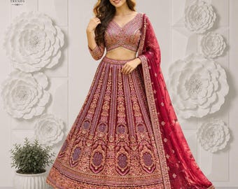 Puede incluir: Un conjunto de lehenga choli color granate con intrincados bordados en oro y rosa, que incluye una blusa con cuello en V, una falda voluminosa hasta el suelo con patrones detallados y una dupatta transparente a juego, marca Karo Trends.