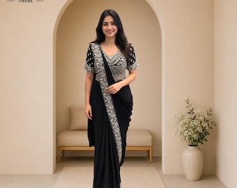 Puede incluir: Un sari negro que presenta una blusa de manga corta con intrincados bordados blancos. La prenda incluye un borde bordado a juego que recorre verticalmente la parte delantera. El texto Karo Trends es visible en la esquina superior izquierda.