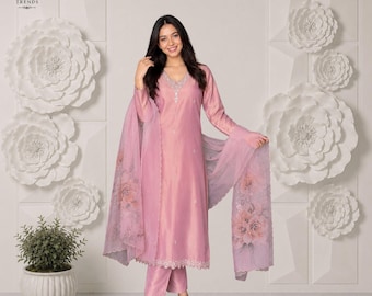 Puede incluir: Un conjunto de tres piezas en color rosa claro que consta de una túnica de manga larga con cuello en V, pantalones rectos a juego y una dupatta ligera y transparente con un estampado floral en los bordes, todo en tela lisa.
