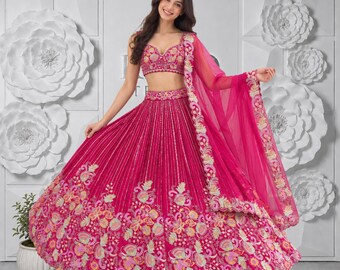 Puede incluir: Un conjunto de lehenga fucsia vibrante que incluye un choli sin mangas con bordados intrincados y una falda voluminosa hasta el suelo adornada con líneas plateadas verticales y un denso borde floral multicolor, junto con una dupatta transparente a juego.