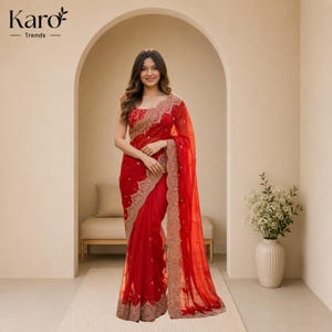 May include: A vibrant red saree featuring intricate gold embroidery along the borders and a matching sleeveless blouse. The fabric is sheer and lightweight, draped elegantly with detailed patterns. The text Karo Trends is visible in the top left corner.