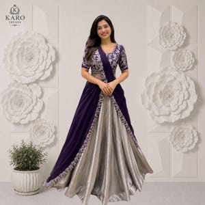 Puede incluir: Un vestido largo hasta el suelo con un corpi&ntilde;o de color morado intenso con bordados plateados y mangas cortas, combinado con una falda fluida de color plata metalizada. Incluye una capa drapeada morada con borde floral plateado.