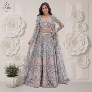 Puede incluir: Un conjunto lehenga verde salvia que presenta un corpi&ntilde;o sin tirantes con escote coraz&oacute;n y una falda larga hasta el suelo, ambos muy adornados con intrincados bordados plateados, lentejuelas y detalles florales en rosa suave, junto con una chaqueta transparente a juego.