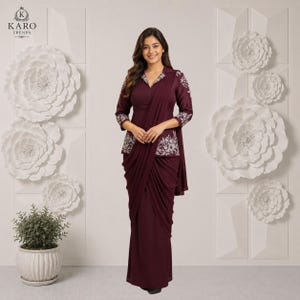 Puede incluir: Un vestido de manga larga en color burdeos intenso con falda drapeada y corpiño estructurado con bordados florales blancos en hombros y cintura. La prenda presenta un escote en V y una silueta entallada, mostrando una mezcla de elementos de diseño tradicionales y modernos.