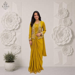 May include: A mustard yellow saree paired with a matching long-sleeved jacket featuring intricate floral embroidery on the front panels. The ensemble includes a solid mustard yellow skirt with a draped pallu and a decorative border at the hem.