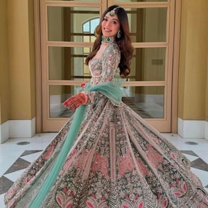Puede incluir: Un lehenga choli largo hasta el suelo con bordados intrincados en tonos verde salvia, rosa empolvado y plata. El conjunto incluye un corpi&ntilde;o ajustado de manga larga, una falda voluminosa con motivos florales detallados y un dupatta verde menta.