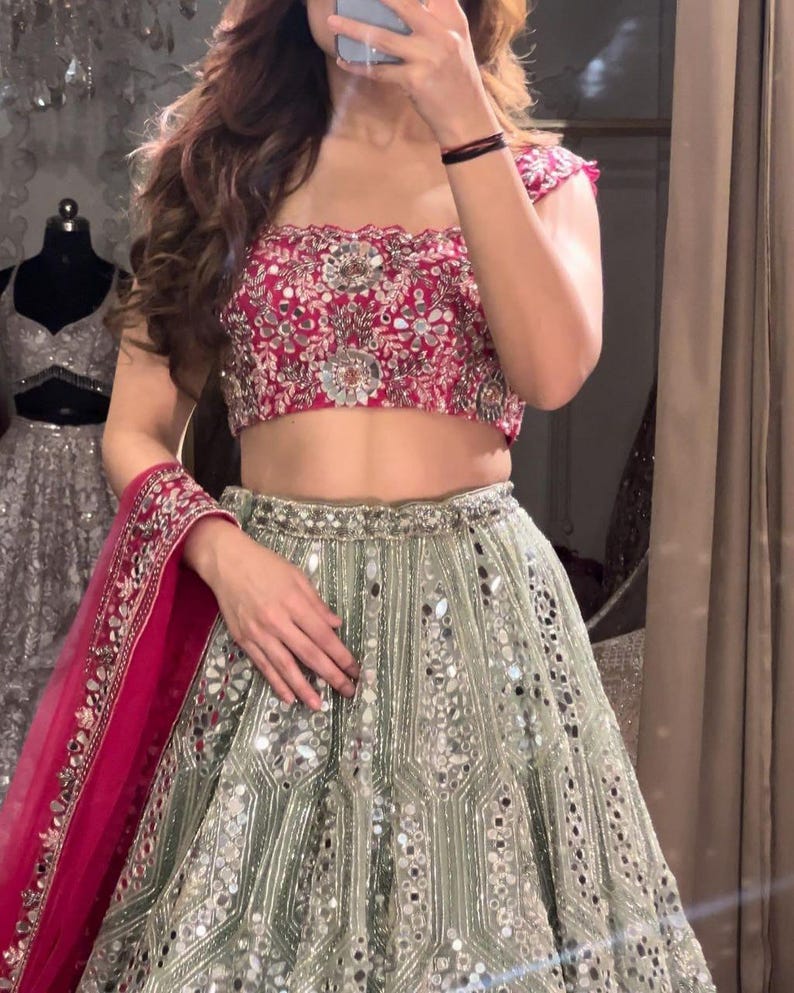 May include: A two-piece ensemble featuring a vibrant magenta cropped top with intricate silver embroidery and mirror work, paired with a high-waisted sage green floor-length skirt adorned with vertical silver embellishments and mirrors.