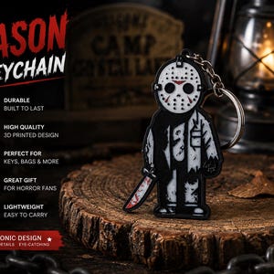 May include: A black and white keychain featuring a stylized character wearing a hockey mask with red markings and holding a blood-stained knife. The text JASON KEYCHAIN is printed in red and white. The design includes a metal ring and chain.