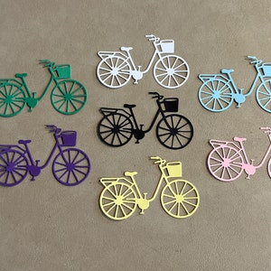 Puede incluir: Siete formas de bicicleta troqueladas en varios colores, incluyendo verde, morado, negro, amarillo y rosa. Cada bicicleta tiene una cesta en el manillar.