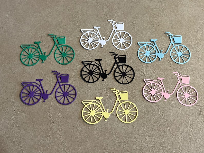 Puede incluir: Siete formas de bicicleta troqueladas en varios colores, incluyendo verde, morado, negro, amarillo y rosa. Cada bicicleta tiene una cesta en el manillar.