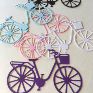 Puede incluir: Cinco recortes de papel de bicicletas en diferentes colores: negro, azul claro, rosa, blanco y morado. Cada bicicleta tiene una cesta y un dise&ntilde;o detallado.