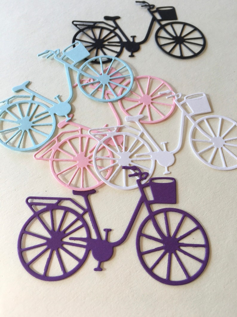 Puede incluir: Cinco recortes de papel de bicicletas en diferentes colores: negro, azul claro, rosa, blanco y morado. Cada bicicleta tiene una cesta y un dise&ntilde;o detallado.