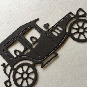 以下が含まれることがあります： 4 つの車輪が付いたヴィンテージカーの黒い金属製ダイカット。車は丸みを帯びた屋根と長方形のボディを持つ詳細なデザインです。