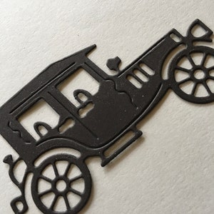 以下が含まれることがあります： 4 つの車輪が付いたビンテージカーの黒い金属製ダイカット。車は丸みを帯びた屋根と長方形のボディを持つ詳細なデザインです。