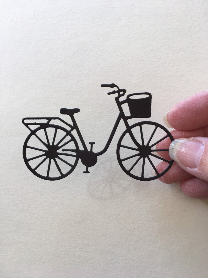 Puede incluir: Silueta negra de una bicicleta con una cesta en el manillar. La bicicleta tiene un dise&ntilde;o cl&aacute;sico con un cuadro curvo y ruedas de radios.