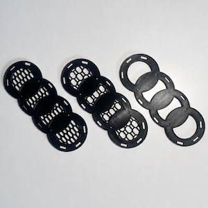 以下が含まれることがあります： 4つの円が連結したデザインの黒いプラスチック製エンブレム3個セット。2つのエンブレムは円の内側に格子状のテクスチャが施されており、もう1つは4つの円が中空のオープンタイプになっています。