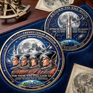 Op de afbeelding: Twee ronde herdenkingsmunten met thema's over ruimteverkenning. Eén munt toont vier astronauten met helmen en de tekst 'CREWED LUNAR MISSION'. De andere toont een raket met de inscriptie 'RETURN TO THE MOON' en 'AFTER 54 YEARS'.