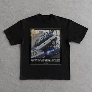 Könnte beinhalten: Ein schwarzes Kurzarm-T-Shirt mit einem Grafikdruck, der ein silbernes Auto zeigt, das auf einem blauen Auto geparkt ist. Die Grafik enthält ein goldenes Auszeichnungssymbol und den weißen Text CAN PARALLEL PARK sowie SOMETIMES darunter.