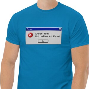May include: A bright blue short-sleeved t-shirt featuring a graphic print of a computer error window. The graphic displays a red circle with a white X, the text Error 404: Motivation Not Found, and a button labelled OK in a grey box.