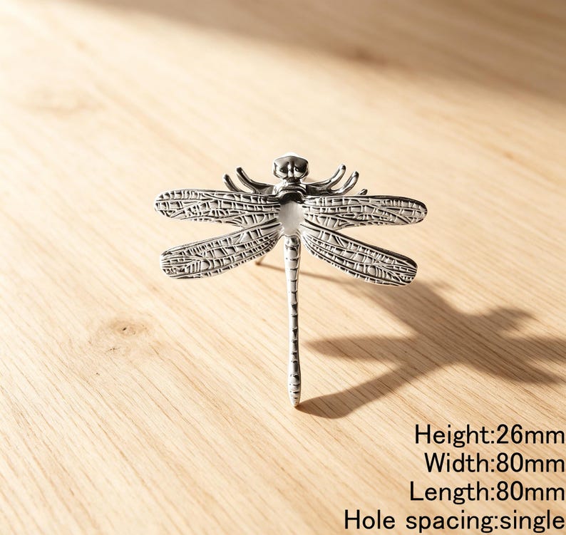 Peut inclure: Un bouton de meuble en forme de libellule de couleur argent&eacute;e avec des d&eacute;tails d'ailes complexes. La quincaillerie pr&eacute;sente une hauteur de 26 mm, une largeur de 80 mm, une longueur de 80 mm et un espacement de trou unique pour le montage.