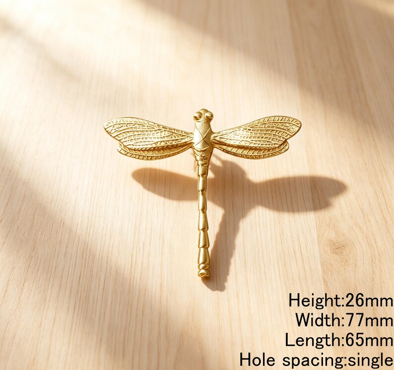 Peut inclure: Un bouton de meuble dor&eacute; en forme de libellule avec des ailes textur&eacute;es et un corps segment&eacute;. La quincaillerie pr&eacute;sente une hauteur de 26mm, une largeur de 77mm, une longueur de 65mm et un espacement de trou unique pour le montage.