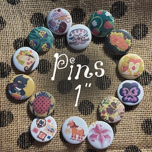 May include: A collection of fourteen circular 1-inch pins arranged in a circle, featuring various colourful illustrations including a moth, a ladybug, a black cat, a horse, strawberries, flowers, and sewing supplies, with the text Pins 1" in the centre.