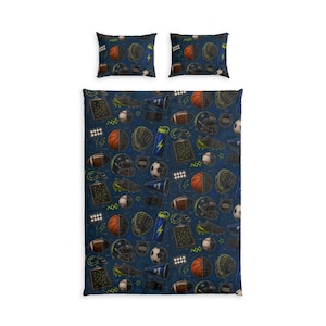 Op de afbeelding: Een donkerblauw beddengoedset bestaande uit een dekbedovertrek en twee kussenslopen met een herhalend patroon van sportuitrusting, waaronder basketballen, voetballen, helmen, voetbalschoenen, megafoons en tactische schema's.