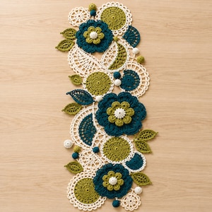 May include: A long, narrow crochet table runner featuring a repeating pattern of large dark teal flowers with olive green centers, circular olive green motifs, and intricate white lace doilies. Small olive green and white crochet spheres are interspersed.