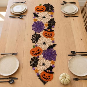 Peut inclure: Un chemin de table en crochet sur le thème d'Halloween composé de citrouilles orange, certaines portant des chapeaux de sorcière violets, entremêlées de toiles d'araignée noires et violettes, de toiles crème avec de petites araignées et d'étoiles orange.